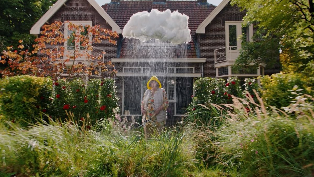 A woman in a rain jacket stands in her garden under a small rain cloud