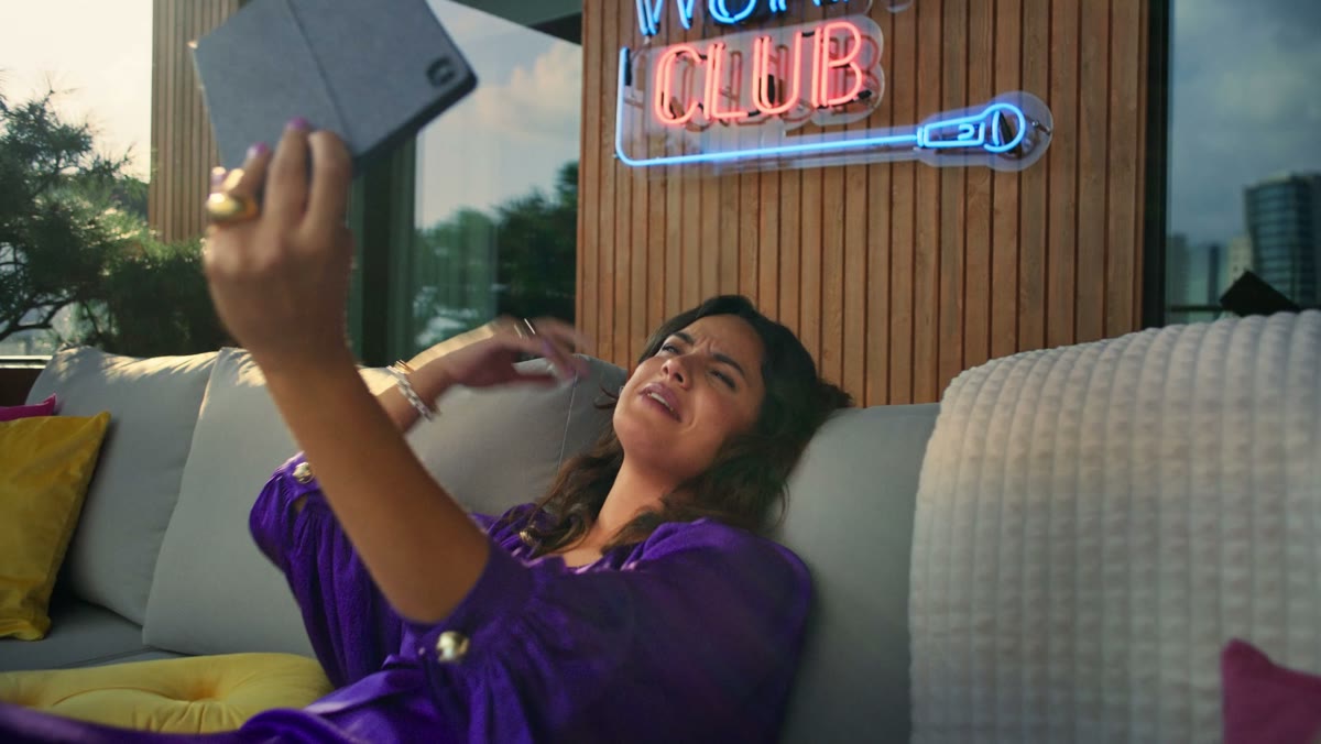 A woman on a purple sofa under an After Work Club neon sign